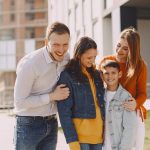Delighted family in trendy casual wear holding each other and standing near modern building on city street while walking together during weekend
